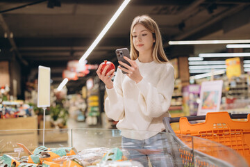 Customer using smartphone comparing pomegranate prices in supermarket
