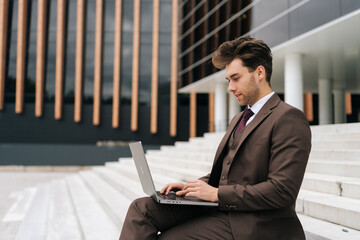 Serious ambitious young professional businessman in sleek suit diligently working on laptop...