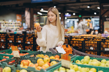 Woman choosing apples in supermarket holding shopping list