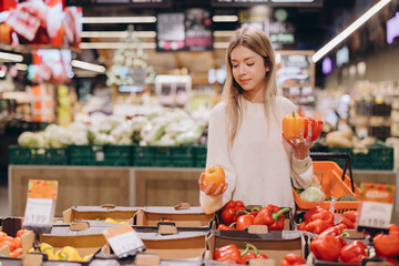 Woman choosing bell peppers in supermarket produce section