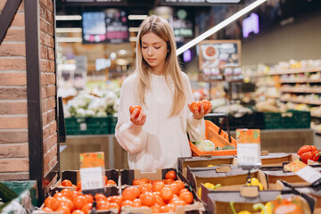 Woman choosing tomatoes in supermarket produce section