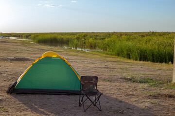 Evening landscape. Tourist tent on the shore of a lake overgrown with reeds at sunset. Travel and tourism