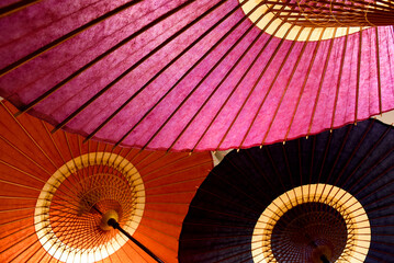 These are colorful Japanese umbrellas made of washi paper. They feature wooden frames and vibrant shades of red, pink, and black, showcasing traditional craftsmanship.