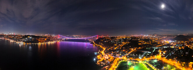 Obraz premium Panoramic Istanbul's Bosphorus Bridge at Night: A Stunning Aerial View. A breathtaking aerial view of Istanbul's Bosphorus Bridge illuminated at night, showcasing the city's vibrant lights reflecting 