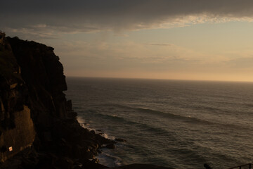 The dramatic cliffs stand tall against the vast calm ocean The sky is a tapestry of clouds bathed in the soft glow of the setting sun