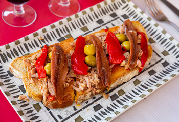 Delicious toasts with shredded canned tuna, anchovies, roasted bell pepper slices and olives. Mediterranean appetizer
