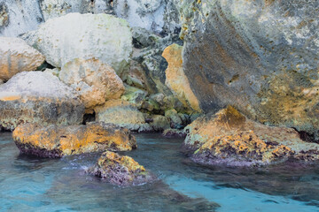 Sharp rocks in a cliff shore formation in turquoise transparent water in Mediterranean beach in Italy