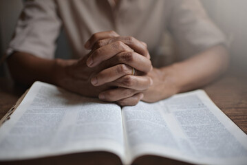 close up on the hands of an unrecognizable man reading the bible and praying. Concept of...