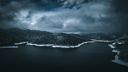 Lake during winter with trees covered in snow and dark skies