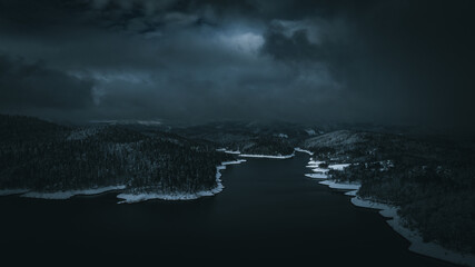 Lake during winter with trees covered in snow and dark skies