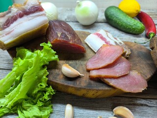 Dried meat and lard on a cutting board surrounded by vegetables.