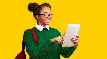 Online Education. Smiling afro teenage girl using digital tablet isolated over yellow studio...