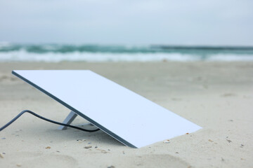 A Satellite Dish rests on the sandy beach under cloudy skies, blending nature and technology