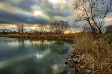 Beautiful landscape with lake and big and smooth clouds in the sky , autumn season, water and trees . Reflections on the water , stormy clouds in the sky . Photography in the forest iwith lake .