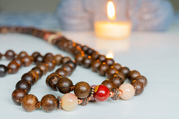 A close up image of a stand of wooden mala beads with lit prayer candle on a white background.