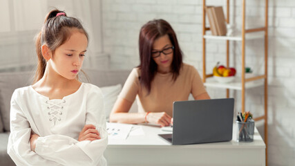 Upset teen girl taking offence at her busy working mother during covid-19 lockdown, copy space. Cute kid feeling neglected and lonely with her mum working online from home