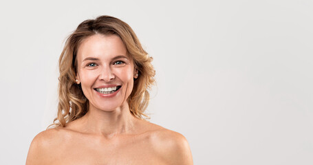Fototapeta premium Natural Beauty. Portrait Of Attractive Smiling Middle Aged Woman With Naked Shoulders Posing Over Light Grey Studio Background, Happy Nude Beautiful Female Looking At Camera, Panorama With Copy Space