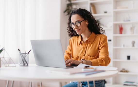 Middle Eastern Lady Using Laptop Working Online Wearing Eyewear Sitting At Workplace In Modern Office. Remote Job, Technology And Career Profession Concept. Side View