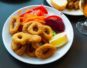 Delicious seafood.Squid salad with calamari rings cooked in deep fryer,lemon,beetroot served on white ceramic plate in sea food restaurant for dinner.Tasty Mediterranean cuisine