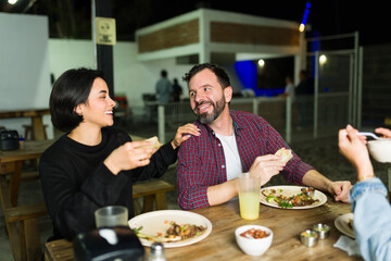 Friends enjoying a meal at an outdoor mexican taqueria, eating tacos and chatting happily