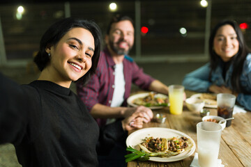 Cheerful millennial friends taking a selfie while enjoying tacos and drinks at a taqueria