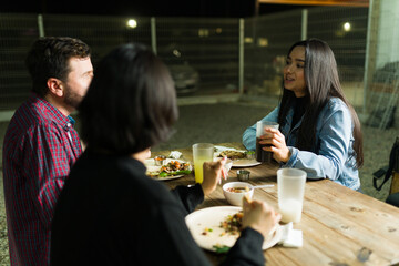 Friends sharing a meal of tacos and drinks at an outdoor taqueria, talking and enjoying each other's company at night