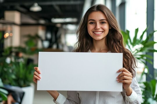 Smiling young woman holding a blank white placard ready for custom message in a business environment