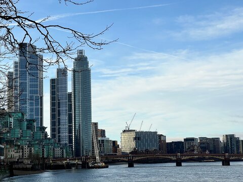Nine Elms, London, United Kingdom - 15th December 2024 - Close-up view of modern glass towers and construction cranes along River Thames, with Vauxhall Bridge in winter light.