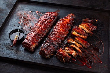Barbecue spareribs St Louis cut with hot rub and BBQ sauce served as close-up on a rustic black...