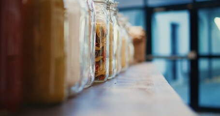 Selective focus of bulk products stored in recyclable jars used to support sustainable lifestyle and vegan nutrition. Zero waste farmers market to lower climate impact. Tripod shot. Close up.