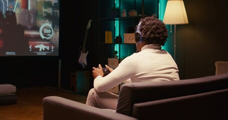 African american man plays videogame on big TV with automatic gun shooting laser bullets at flying robotic foes. Gamer partakes in PvP online multiplayer game tourney on television set, panning shot