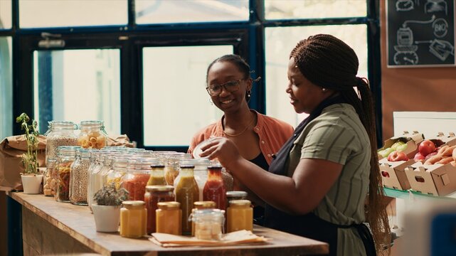 Vendor giving fresh homemade sauces to customer, recommending ethically sourced additives free goods. African american client examining organic natural products at local store.