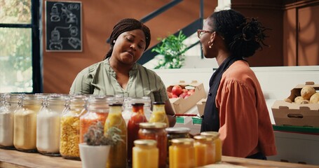 Vendor showing homemade sauces and dressings to buyer, promoting vegan nutrition and healthy lifestyle. Retailer presenting natural bulk items at local grocery store. Handheld shot.