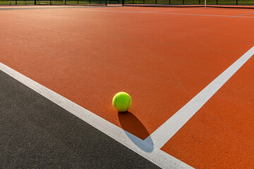 Photo of a yellow tennis ball on orange and black tennis court - pickleball court with white baseline and black out of bounds	