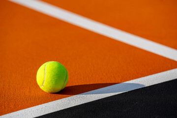 Yellow tennis ball on orange and black tennis court - pickleball court with white baseline and black out of bounds	