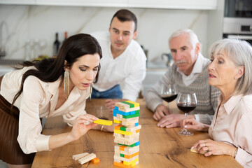 Happy mature and young family members sitting at table with a glass of wine while playing with bricks at home