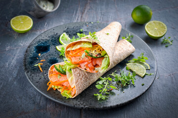 Italian style wrap piada tortilla with cured graved salmon, salad and zucchini served as top view with avocado sour cream dressing dip on a Nordic Design plate
