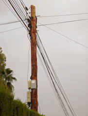 Wooden public utilities pole with tangled electrical wires, equipment and communication boxes...