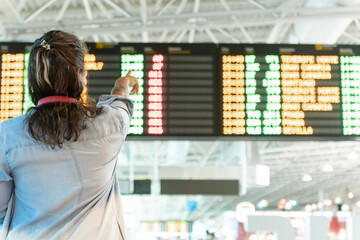 Traveler points at flight information board in bustling airport