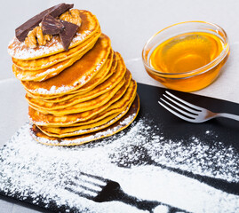 Stack of sweet pancakes with with honey, chocolate and powdered sugar at plate