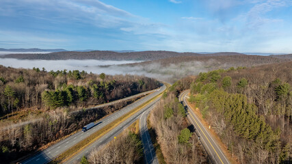 Nearly empty highway on a sunny day descending into thick fog, cloud cover, creating a mysterious and serene landscape.
