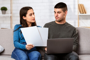 Couple filling online form on website, checking information with papers, analyzing bank loan conditions