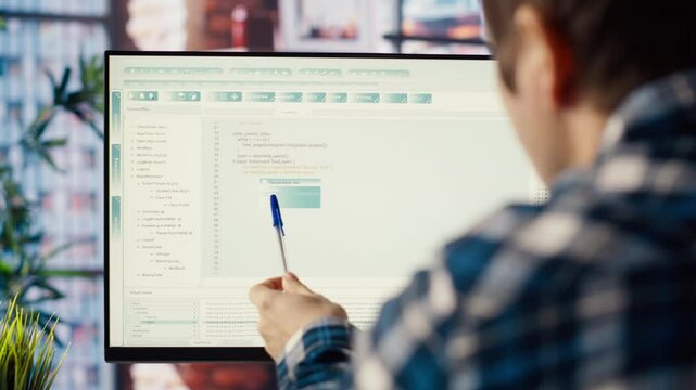 Programmer at desk typing code, developing software programs, entering commands. Man in home office fixing errors in application, implementing new features pointing to code with pen, camera B