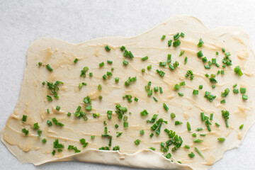 Overhead view of raw chinese scallion pancakes being rolled on white countertop, top view of homemade scallion pancakes, process of making cong you bing
