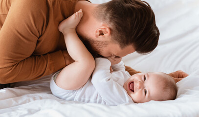 Father's Love. Dad Cuddling Bonding With Little Baby Son Spending Time Together Lying On Bed At Home. Loving Daddy Laughing Playing With Cute Toddler. Fatherhood, Parenting Joy And Child Care