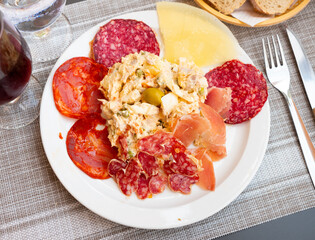 Appetizing Russian salad Olivier garnished with olive served with slices of Spanish sausages, cured jamon and cheese. Traditional tapa
