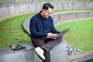 Obraz premium Smiling Man In Semi Formal Clothes Working Using Laptop While Sitting on Bench