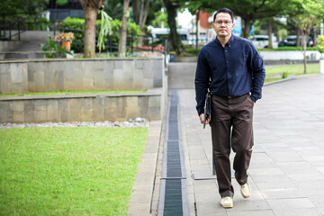 Portrait Of Businessman Walking on Park While Holding Laptop