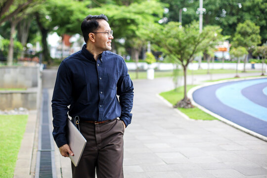 Portrait Of Businessman Walking on Park While Holding Laptop