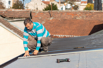 Roofer assembles sheet metal on the roof. Construction workers - installation assembly of new roof. Roofing tools.